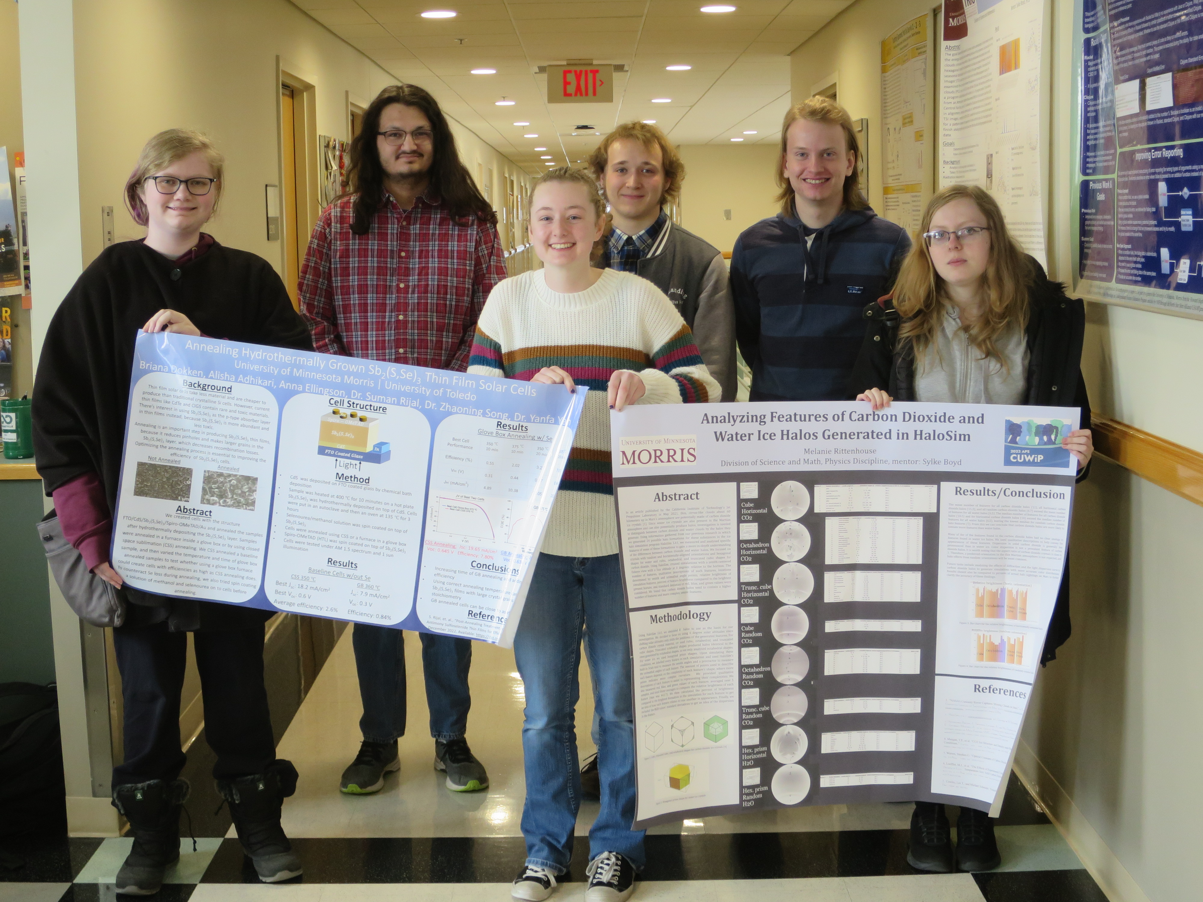 Six people standing in a hallway, holding two scientific posters