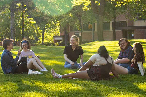 Six students sitting on the grass on the campus mall