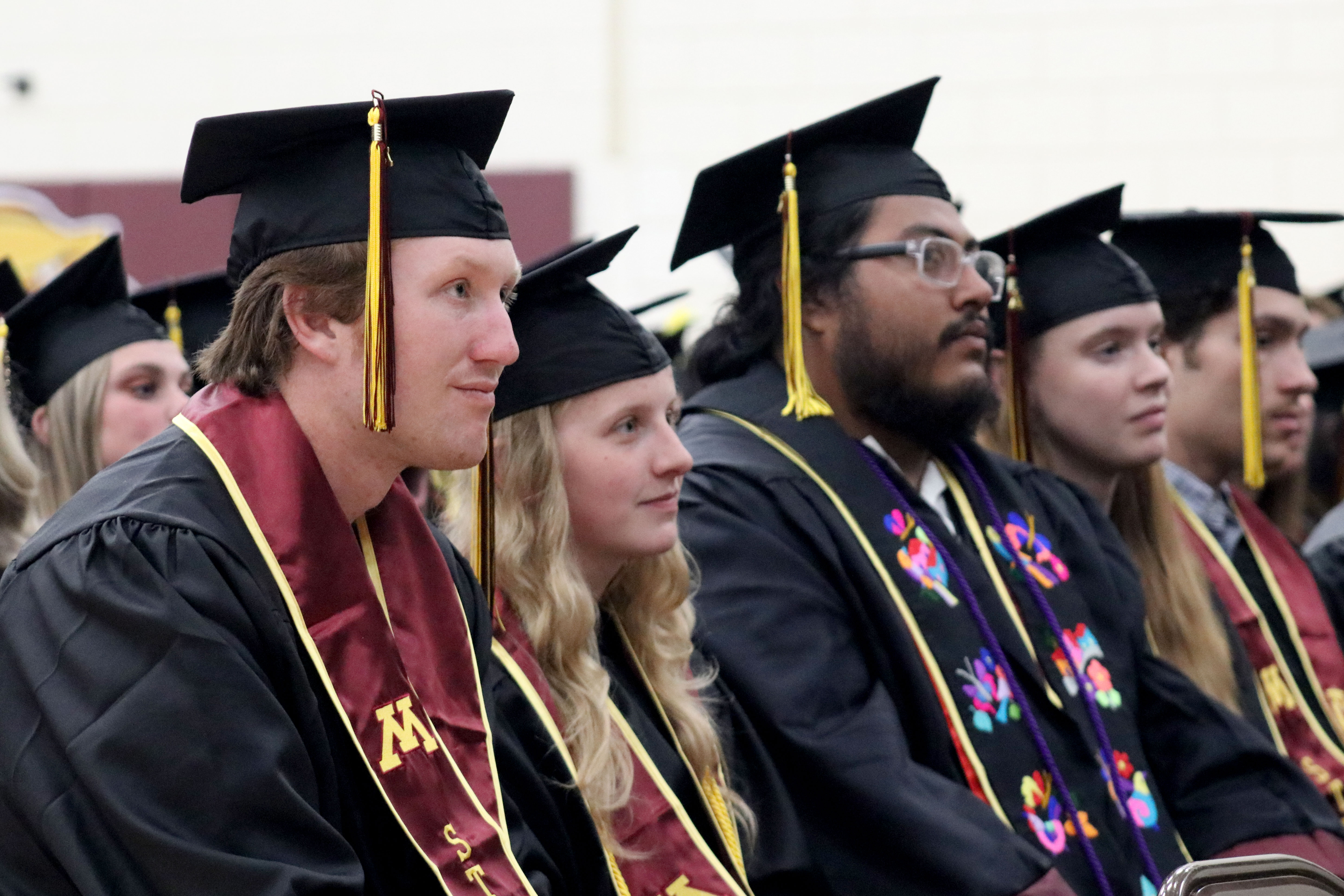 Graduates in caps and gowns listening to a speech at a commencement ceremony.