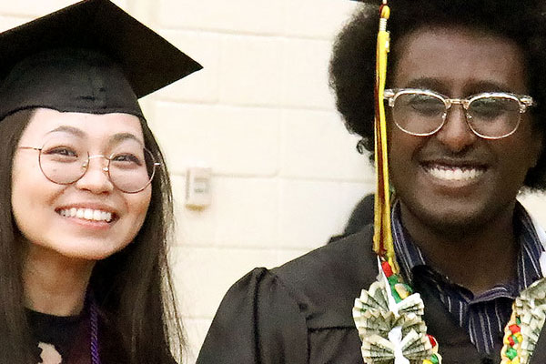 Two students in graduation attire in line to receive their diplomas