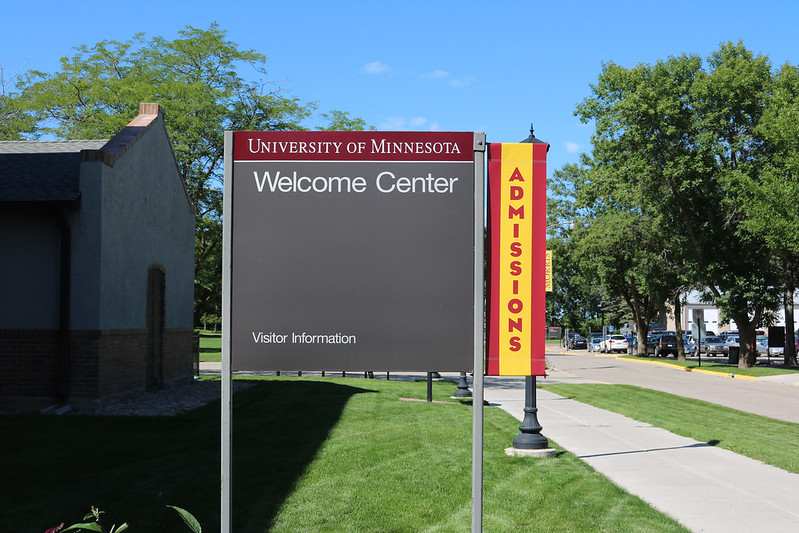 A metal sign for the Welcome Center with a maroon and gold banner on the side that reads, Admissions