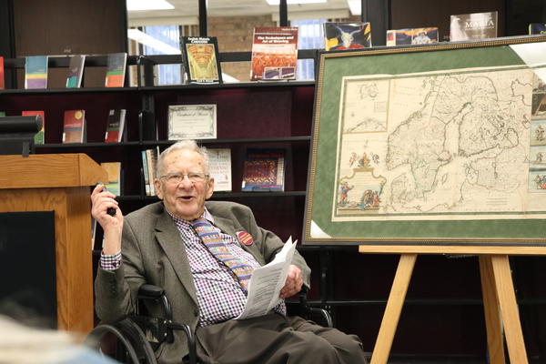 A man seated in a wheelchair next to a framed map