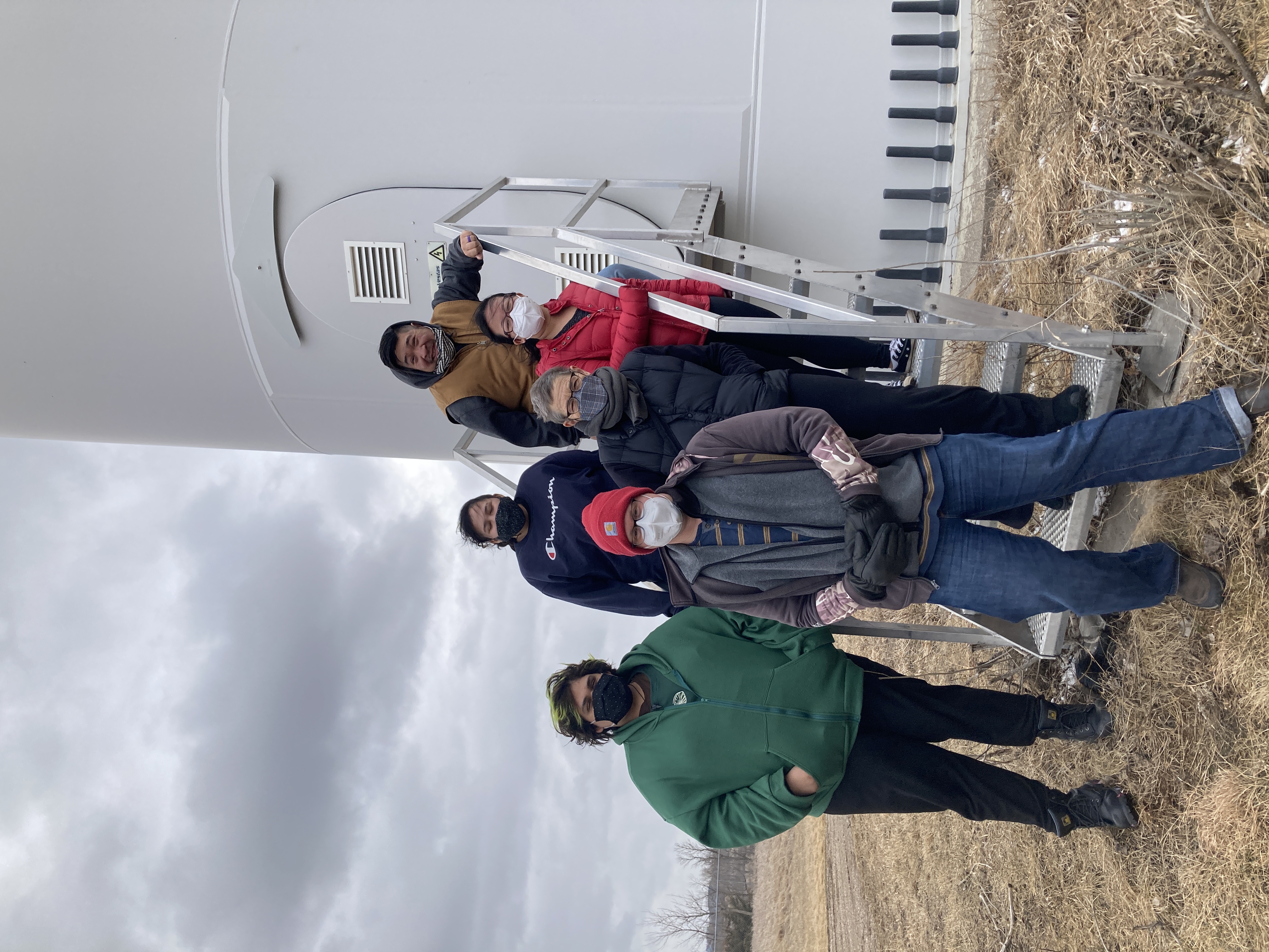 Six people standing outside on a staircase into a wind turbine. 