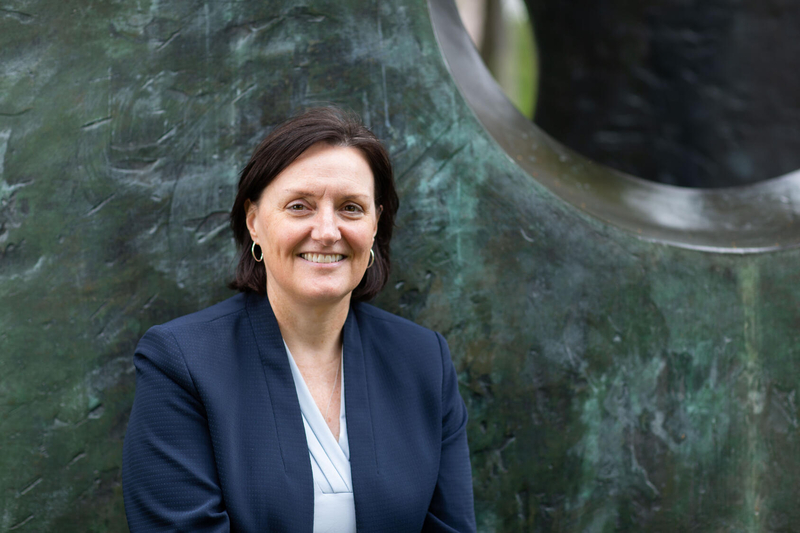 A woman with short dark hair, wearing a navy blue blazer and white shirt