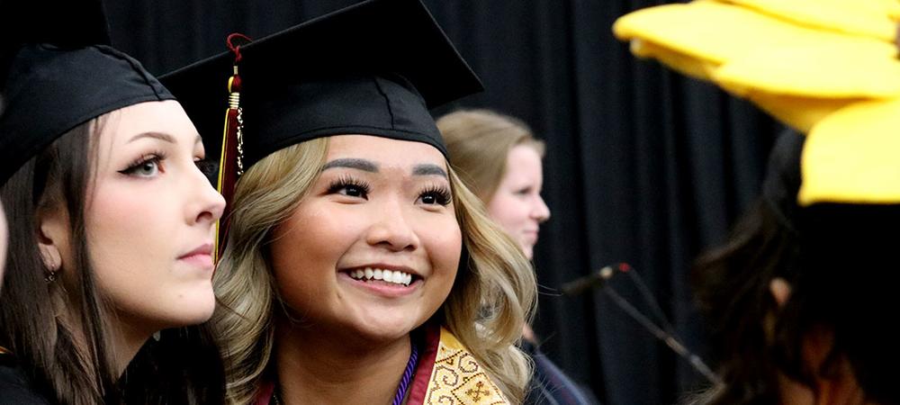 Graduates at commencement look back at the audience and smile