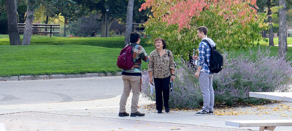 Two students talk with a faculty member on a sunny fall day on campus.