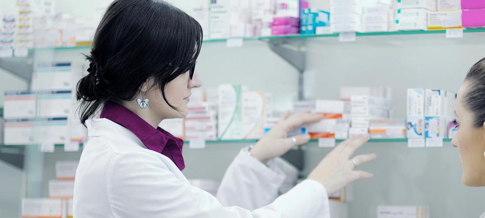 Two women in white coats work in a pharmacy.