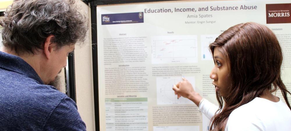A statistics student discusses her research poster with a faculty member.