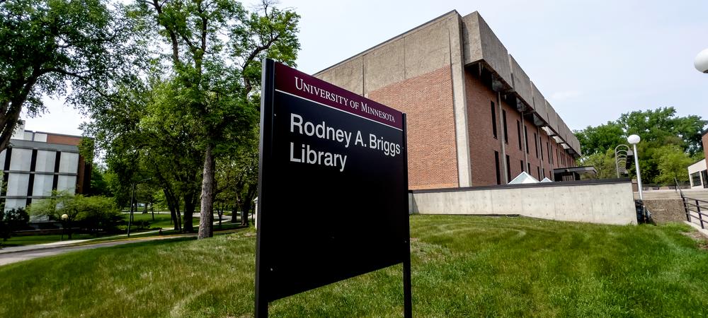A photo of the exterior sign that reads, Rodney A. Briggs Library with a brick building in the backgroud