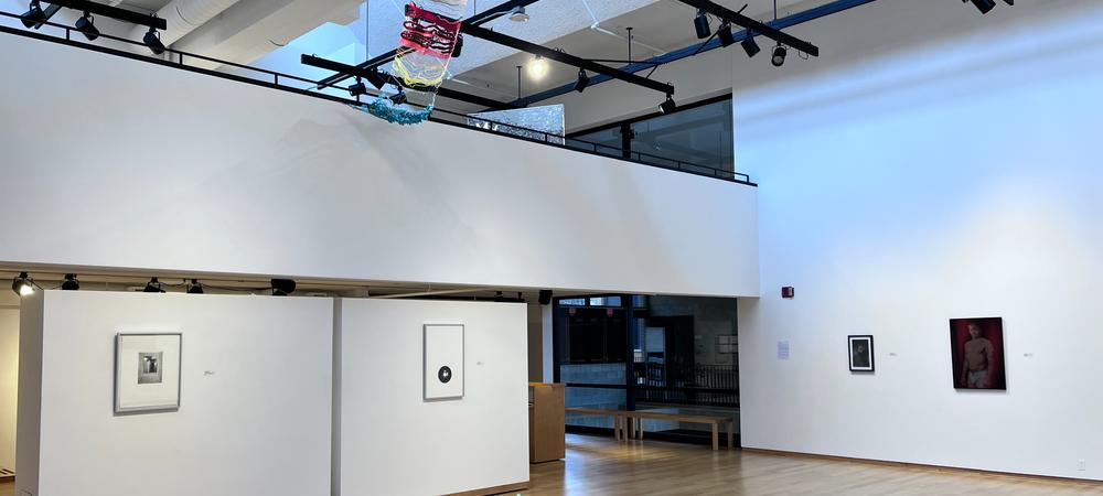 A view of the interior of a gallery with displays on white walls and hanging from the ceiling. 