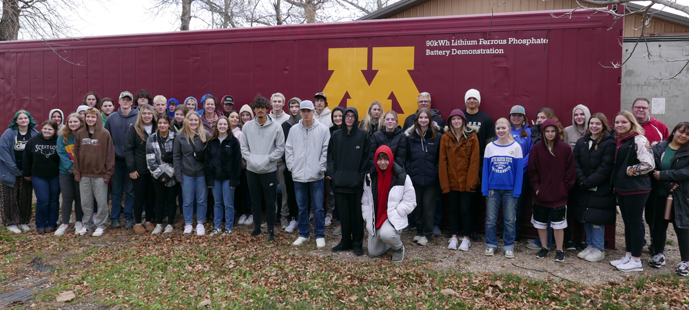 A group of high school students standing in front of a maroon shipping container with a gold M on it