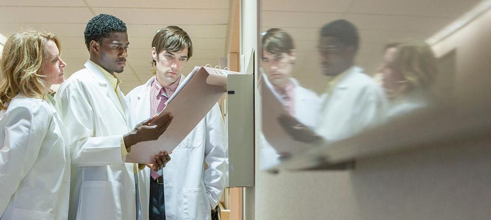 Three people in medical lab coats reviewing a patient chart