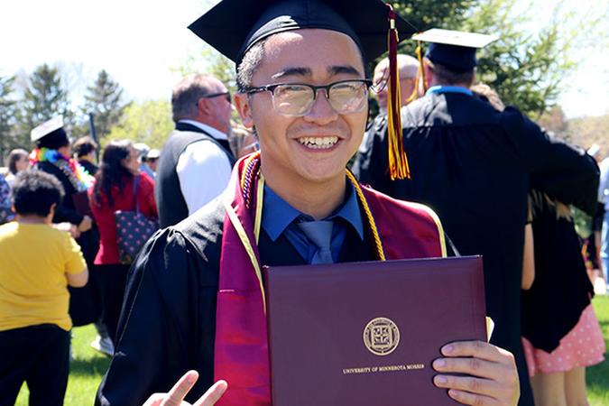 A graduate smiles, holding his diploma