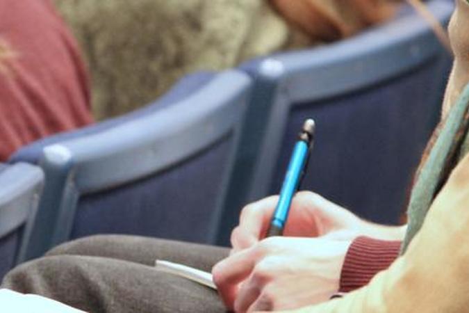 a person sitting with a pencil and notebook in auditorium seatnig