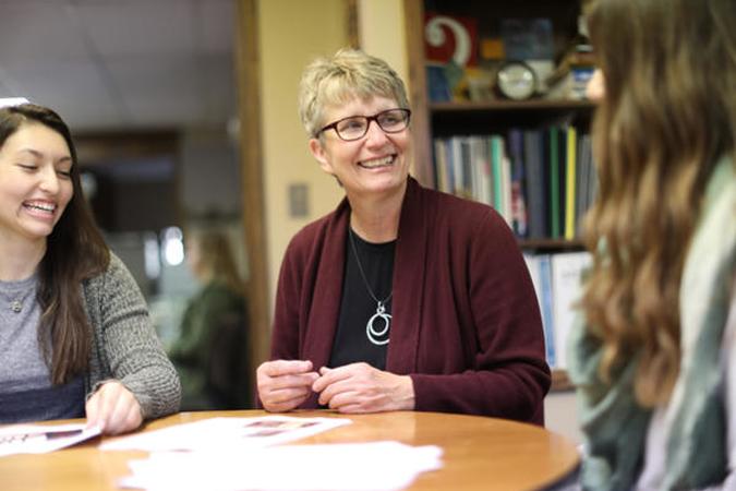 Sandy Olson-Loy, Vice Chancellor for Student Affairs talking with two students around a table