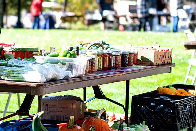 A table full of fresh vegetables and preserves at an on-campus farmers market.
