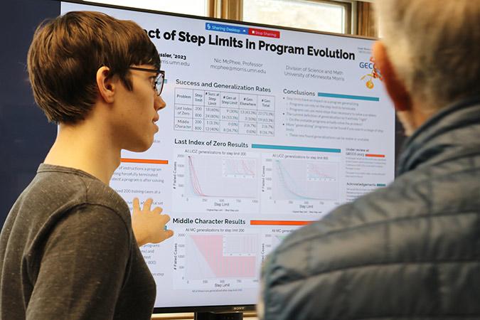 student presenting research poster that features complicated graphs and charts
