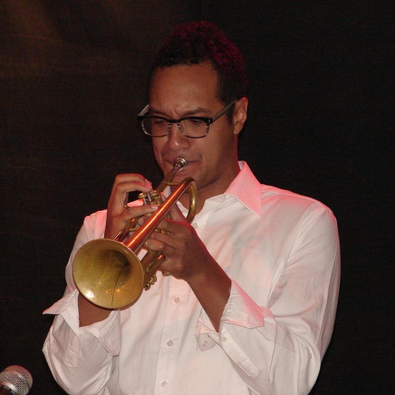 A man with short dark hair, wearing glasses and a white shirt, playing a trumpet