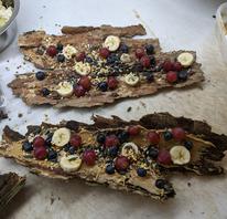 two pieces of bark covered with honey, sliced bananas, grapes and blueberries