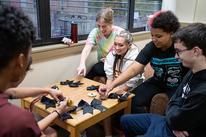 Students gather around a table and create hair bows using black ribbon and glitter glue.