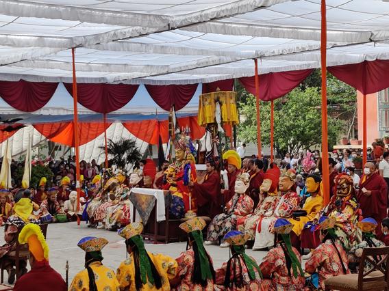 A room filled with people wearing brightly colored outfits, traditional Nepali headwear and some dramatic masks.  