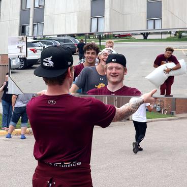 Student holds up mirror, which reflects him and other members of the football team, helping new students move into residence hall.
