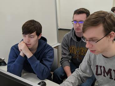 Three male college students sitting at a computer