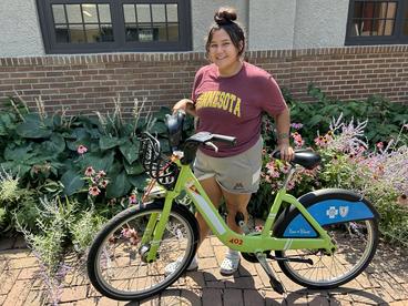 A woman holding a green bike near a flower garden