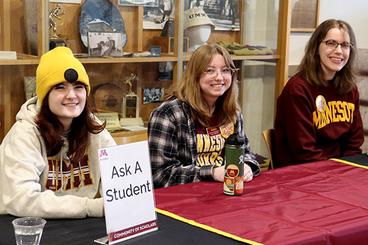 Three students at an "Ask a Student" table at the Community of Scholars January event.
