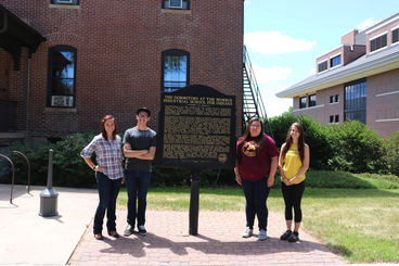 Four students standing outside a historic brick building