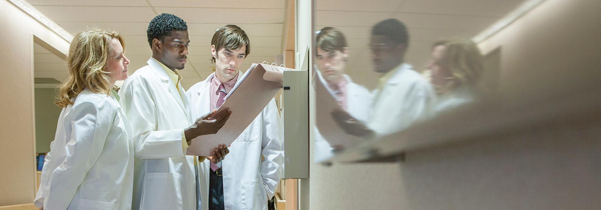 Three people in medical lab coats reviewing a patient chart